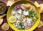 A bowl of pozole with corn chips, lime and salsa.