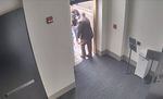 A person exits a door and other people are visible outside the door.