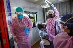People wearing pink medical gowns, gloves and protective masks as they work with a patient who sits in a dental chair inside a large bus or RV.