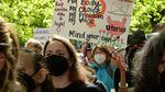 A group of people outdoors and wearing face masks appear to be angry, and one holds a protest sign reading, "My body, my choice, my freedom, my voice, mind your own uterus."