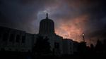 The Oregon Capitol forms a dark silhouette against a pink and blue sky with gray clouds.