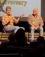 Two men sit on a stage at a convention.