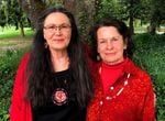 Two women, both wearing red, stand side by side at a park in front of a tree. They organized an event to recognize murdered and missing Indigenous women and girls.