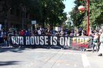 a large group of people march behind a banner some are carrying, which reads, "OUR HOUSE IS ON FIRE"