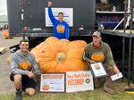 In this photo provided by The Great Pumpkin Farm, Emmett Andrusz, from left, Steve Andrusz and Scott Andrusz, pose with the record-setting 2,554-pound pumpkin in Clarence, N.Y., on Saturday.