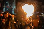 A man spits fire on a torch as other people walk close by.