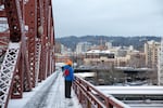 A pedestrian looks out over a snow-covered Portland, Ore., from the Broadway Bridge Tuesday, Feb. 5, 2019.