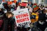 A demonstrator carrying a sign that says “VOTING RIGHTS NOW” walks across the Frederick Douglass Memorial Bridge in 2022 in Washington, D.C.