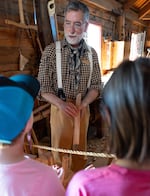 Jay Schindler, a volunteer history reenactor, explains how he uses a plane, used to make flat, straight pieces of wood for furniture to two young children, giving them shavings of wood at Fort Vancouver in Vancouver, Wash., on July 3, 2026. 