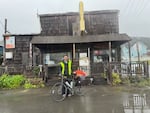 A man in a fluorescent vest stands in front of a brown store with his bike.