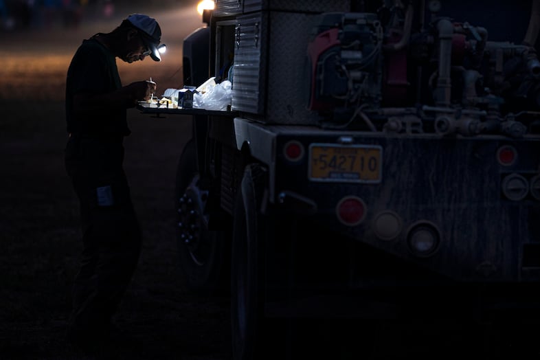 A person wears a headlamp and sits in a dark room eating at a table.
