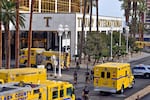 Yellow fire vehicles and personnel in uniforms surround the valet area where a Tesla Cybertruck caught fire at the Trump International Hotel in Las Vegas. Tall palm trees stand around the hotel.