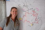 Logistics Section Chief Cindy Wedekind poses next to one of the many giant maps outlining the current shape of the fire. Hundreds of these maps might be printed every day for each team in the camp, and out on the fire.