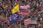 Supporters listen as President Donald Trump speaks as a Confederate-themed and other flags flutter in the wind during a rally in Washington.