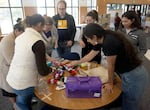 More than a half dozen people huddle around a table to pick from a selection of colorful yarn.