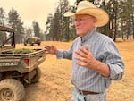 A man in a cowboy hat talking to someone, with his hands outstretched.