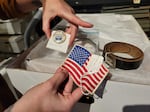 In this undated photo, Springfield History Museum curator Maddi McGraw displays an American flag patch, Springfield Frontier Days button and brown leather belt that have been stored together in a box for several years. The museum is closing for six months to reorganize items in the interest of preserving them as they age.