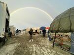 Attendees look at a rainbow over flooding on a desert plain on Sept. 1, 2023, after heavy rains turned the annual Burning Man festival site in Nevada's Black Rock desert into a mud pit.