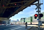 A bicyclist waits for a freight train to pass, in front of a long line of cars (not pictured) in downtown Portland on Friday, May 22, 2026. The train took about 20 minutes to pass over SW Naito Parkway.