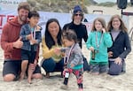 Three adults and three young children pose and smile in the sand before the events stage.