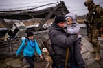 A man carries a child as he helps a fleeing family across a bridge destroyed by artillery, on the outskirts of Kyiv, Ukraine.