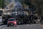 Vehicles drive past a charred bus the day after the Mexican army killed Jalisco New Generation Cartel leader Nemesio Oseguera Cervantes, known as "El Mencho," in Guadalajara, Mexico, Monday, Feb. 23, 2026.