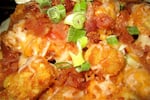 A close-up of tater tots topped with cheese and sliced green onions