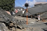 A person walks past the houses collapsed in an earthquake in Yatsushiro, Kumamoto Prefecture, southern Japan, Friday, July 31, 2026.