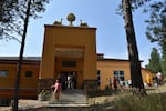 People exit a bright orange Buddhist hall on a sunny, blue sky day.