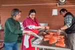 Three people stand around a metal table as they prepare raw salmon.