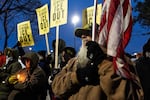 U.S. Navy veteran Earl Netwal, 77, holds a U.S. flag at a vigil while others near him hold signs that say "ICE out."