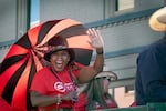 A woman in a red shirt and a black hat inspired by the 1999 film Wild Wild West waves as she holds a red and black umbrella.