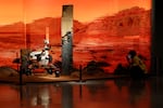 A woman wearing a mask talks on her phone near an exhibition depicting a rover in Mars in Beijing on Friday, May 14, 2021. China says its Mars probe and accompanying rover are to land on the red planet sometime between early Saturday morning and Wednesday Beijing time. (AP Photo/Ng Han Guan)