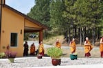 Robed in orange and red cloth, Buddhist monks walk outside Sravasti Abbey.