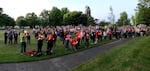 People stand outside in a mown field. Many hold lights in their hands.