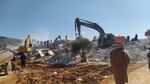 Large machines sort through a pile of rubble as people look on.