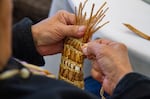An elder tightens the raffia used to weave together thin strips of cedar bark. With each stitch, she is closer to completing her cedar basket.