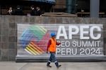 A worker walks past a sign presenting the Asia-Pacific Economic Cooperation (APEC) summit outside the Ministry of Culture in Lima, Peru, Tuesday, Nov. 12, 2024.