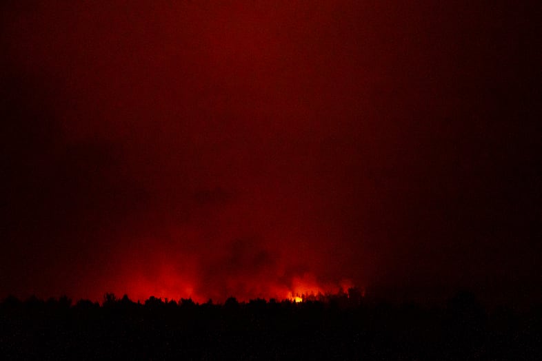 Orange light of a fire is visible through clouds in the distance behind a dark tree or ridgeline.