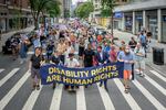 A big crowd of people is marching down a street in New York holding up a banner that says disability rights are human rights in big yellow letters on a blue background.