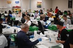 Pairs of election workers from different political parties open and inspect mail ballot envelopes inside the Maricopa County Tabulation and Election Center in Phoenix on Election Day, Nov. 5, 2024.