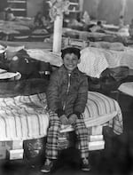 In this image from 1975, a young Vietnamese refugee sits on a cot in the Mount Angel Oktoberfest building.