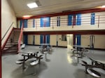 A room with metal tables and inmate cells in the background.
