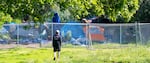 Tents of unsheltered people camping along the Peninsula Crossing Trail are seen through the fencing at the Peninsula Crossing Safe Rest Village, May 18, 2023. The encampment along the trail has since been cleared, but neighbors say the issues seen along the trail are now in the midst of their neighborhood, including theft, open drug dealing, fighting and screaming. 