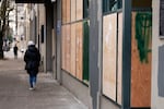 A person walks by the boarded-up windows of the Multnomah County Elections building on Tuesday, Jan. 21, 2025, in Portland, Ore., after a group of people broke dozens of windows and spray painted anti-government graffiti on the building.