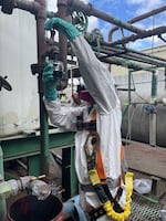 An EPA worker uses a jar to collect fluid from one of the pipes running through the old J.H. Baxter facility.