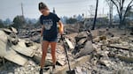 In this OPB file photo from 2020, Madeline Smith walks between what was the living room and laundry room of her house in Talent, Ore, destroyed by wildfires that charred neighborhoods and communities over a devastating summer and fall. Thousands of Oregonians have been displaced events linked to climate change.