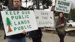 Opponents of a plan to sell the Elliott State Forest hold signs outside an Oregon State Land Board meeting.