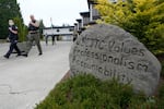 Police officers walk down a sidewalk. A large boulder next to the sidewalk is incribed with the words "WSCJTC values professsionalism accountability int --" the rest of the message on the rock is obscured by a bush.