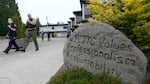 Police officers walk down a sidewalk. A large boulder next to the sidewalk is incribed with the words "WSCJTC values professsionalism accountability int --" the rest of the message on the rock is obscured by a bush.